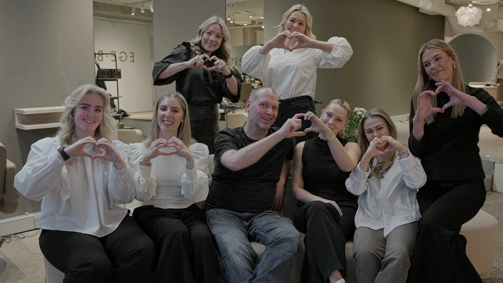 Hele teamet hos Ege & Brørs sitter samlet i salongen og former hjerter med hendene
