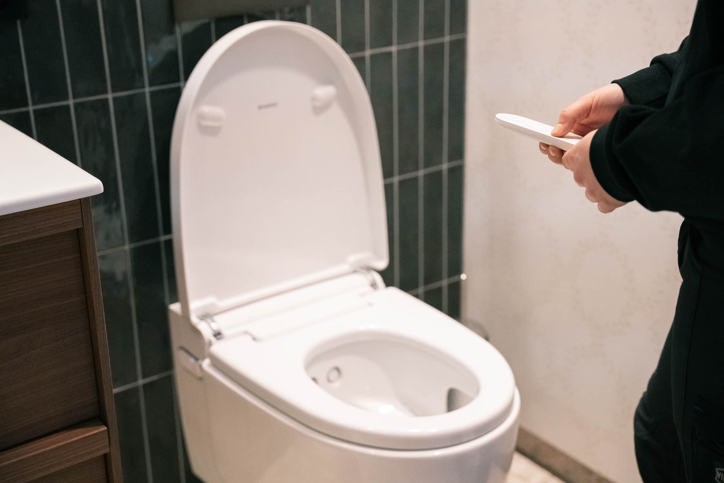 Detaljbilde fra en fotodag hos K. Lund: en hånd holder fjernkontrollen til et dusjtoalett på et ferdig bad