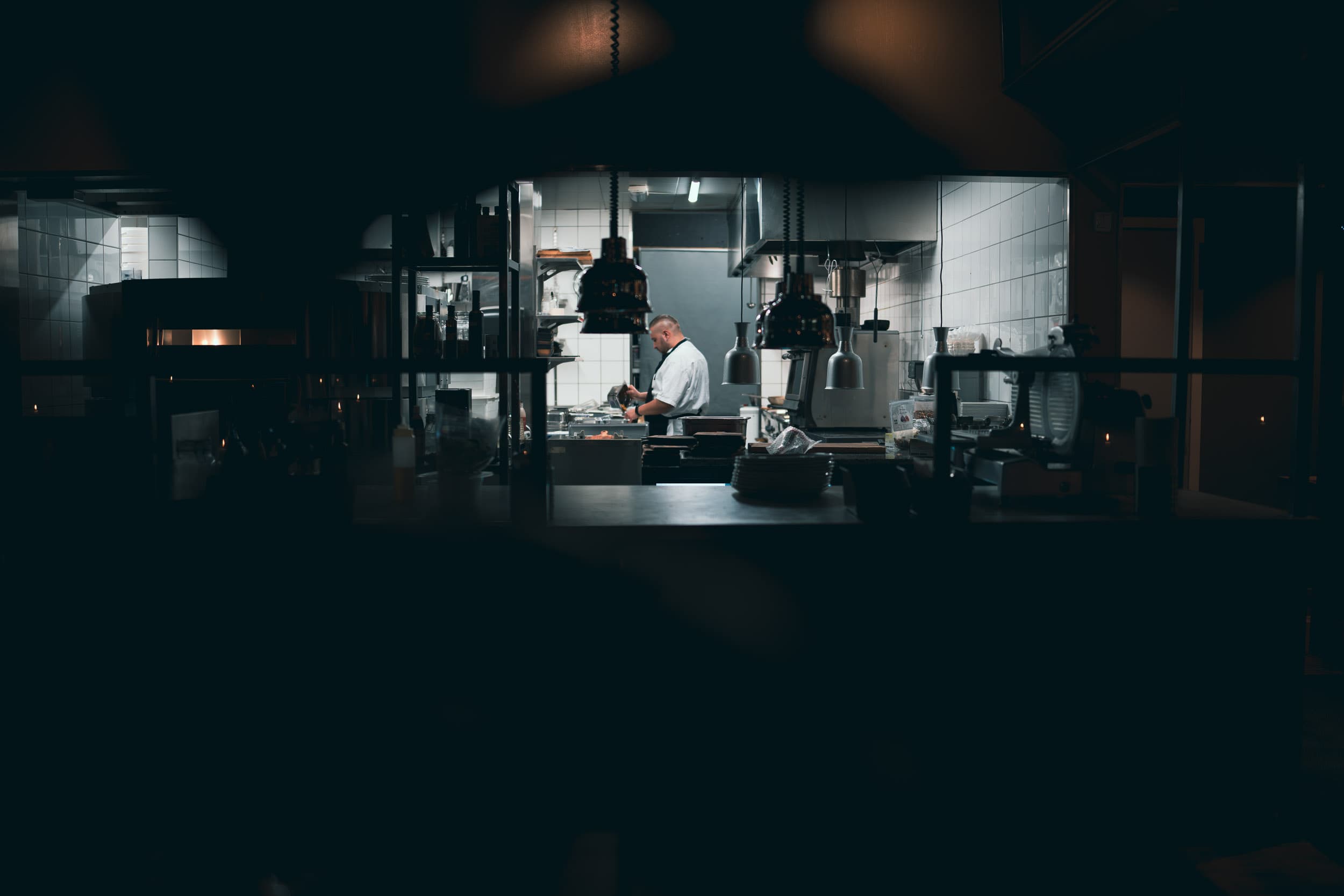 Kokk i det opplyste kjøkkenet hos Frumento, sett gjennom det mørkere restaurantlokalet